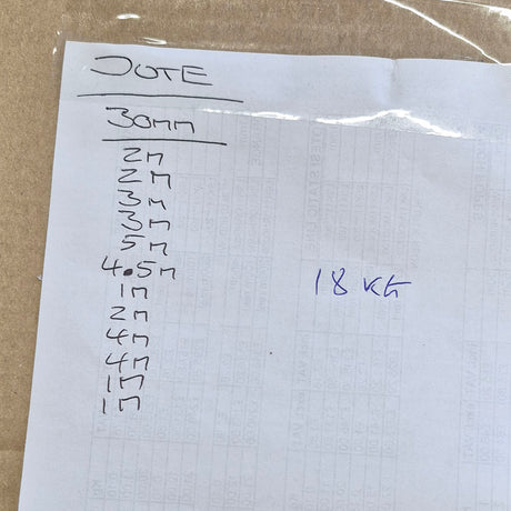 A handwritten note on white paper taped over a brown cardboard surface, listing quantities in meters and writing '18 KG' in blue ink.
