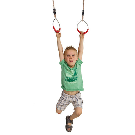 A young child hanging from two gymnastic rings against a plain white background, wearing a green t-shirt and plaid shorts.