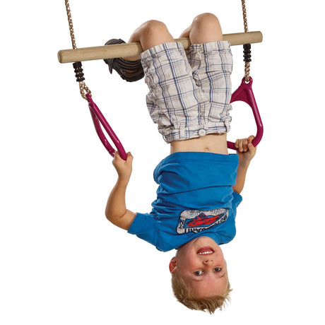 A child hanging upside down from a hardwood trapeze with plastic rings, wearing a blue t-shirt and plaid shorts, isolated on a white background.