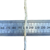 A close-up of a sisal rope, running vertically down the centre of a metal ruler on a white background, to show thickness.